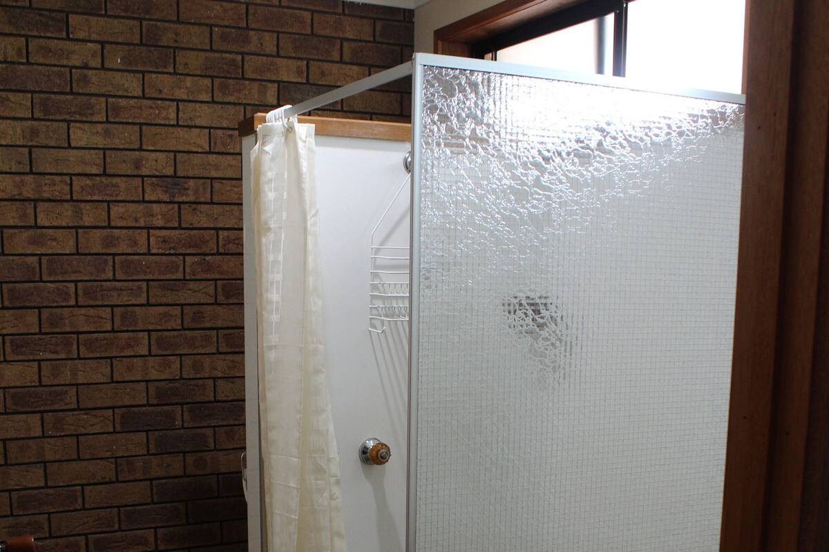 A bathroom with a shower enclosure, a tiled floor, and a brick wall.