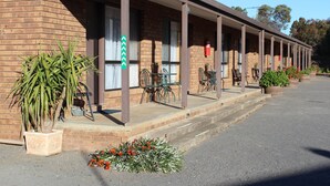 A motel with a brick facade, outdoor seating, and a fire extinguisher mounted on the wall. - Dunolly Golden Triangle Motel (Dunolly)