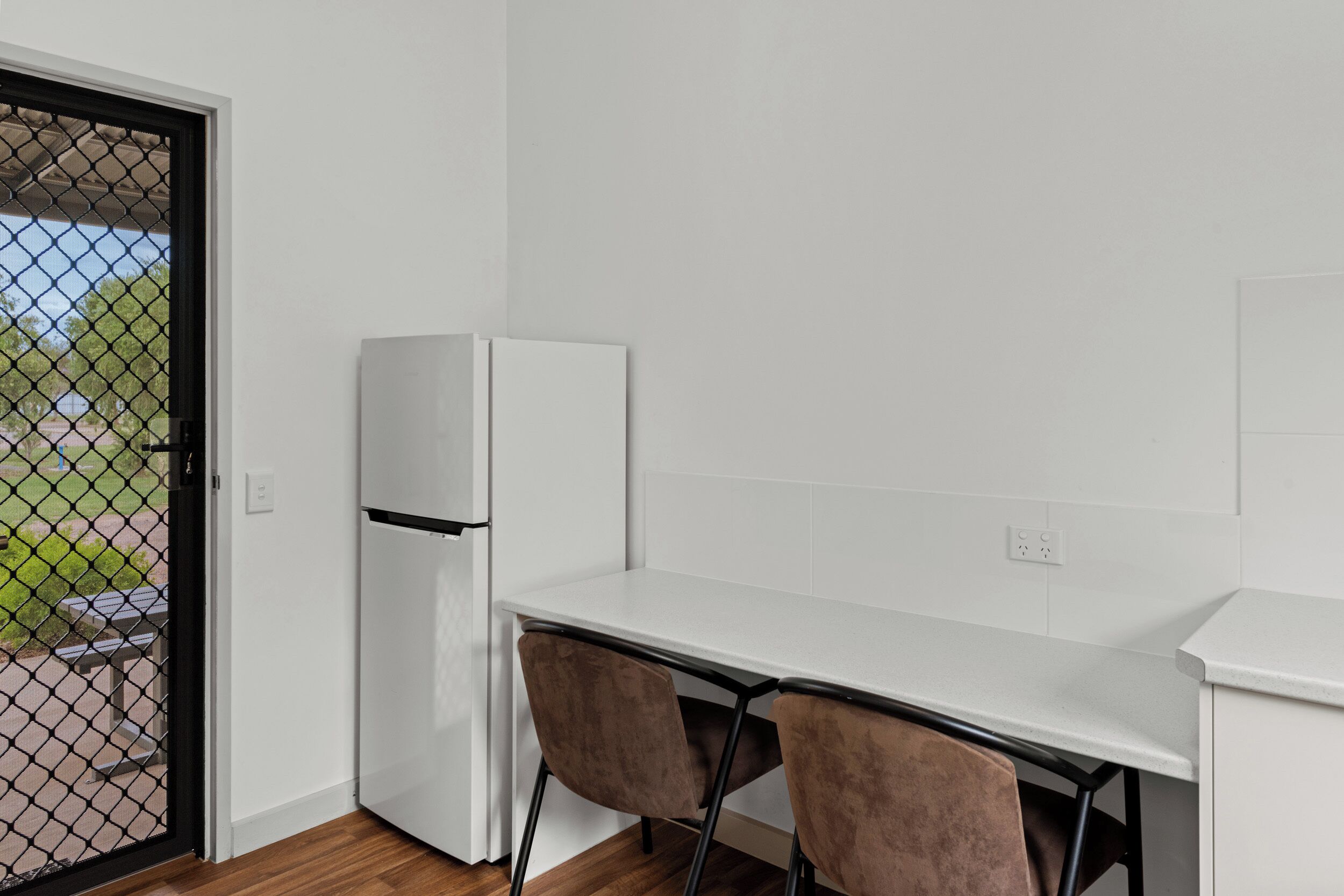 A small kitchenette with a white refrigerator, a white countertop, and two brown chairs.