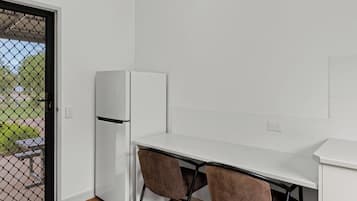 A small kitchenette with a white refrigerator, a white countertop, and two brown chairs.