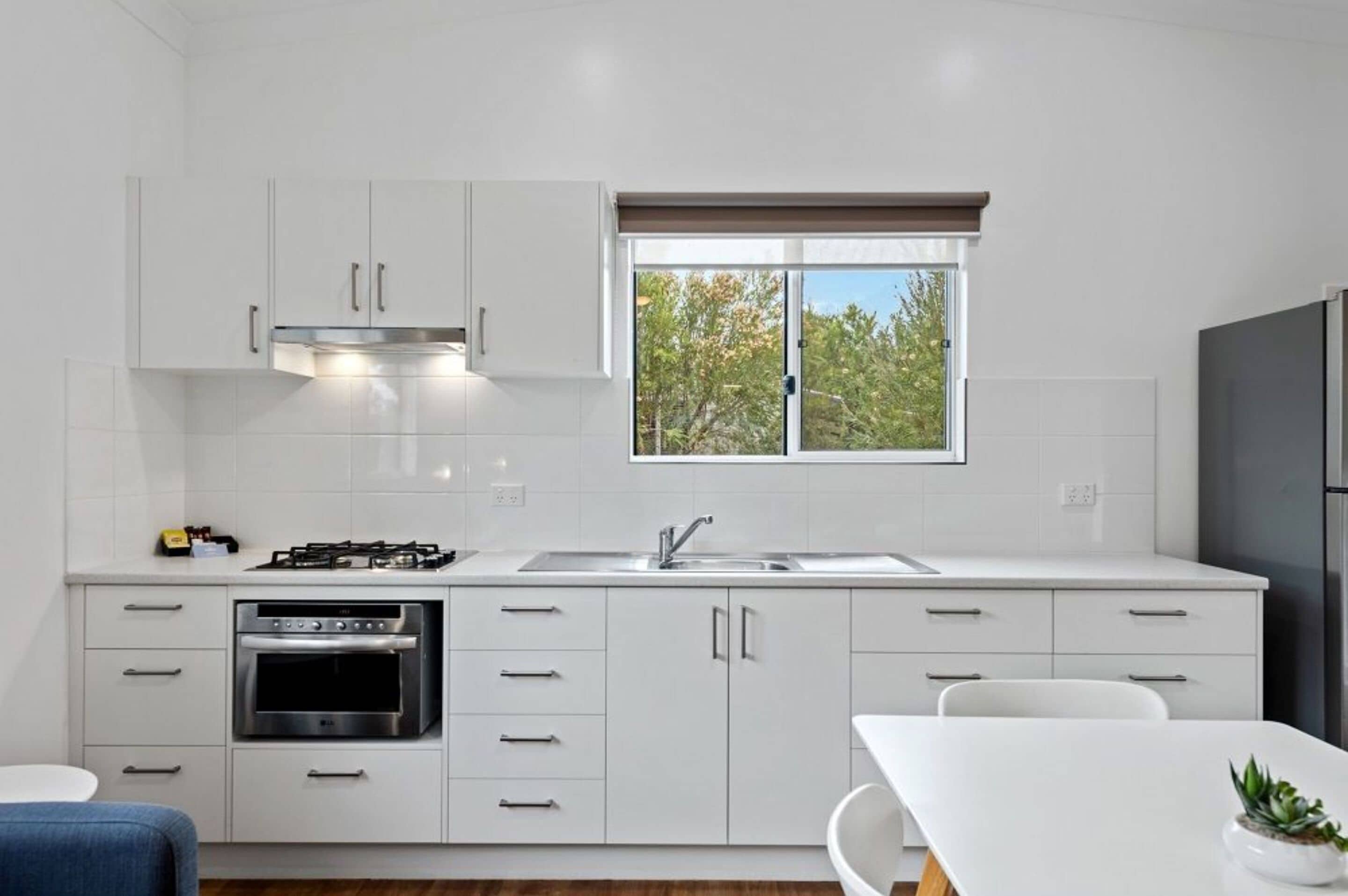 Eine moderne Küche mit weißen Schränken, einem Gasherd, einem Backofen, einer Spüle und einem Fenster mit Blick auf Bäume.
