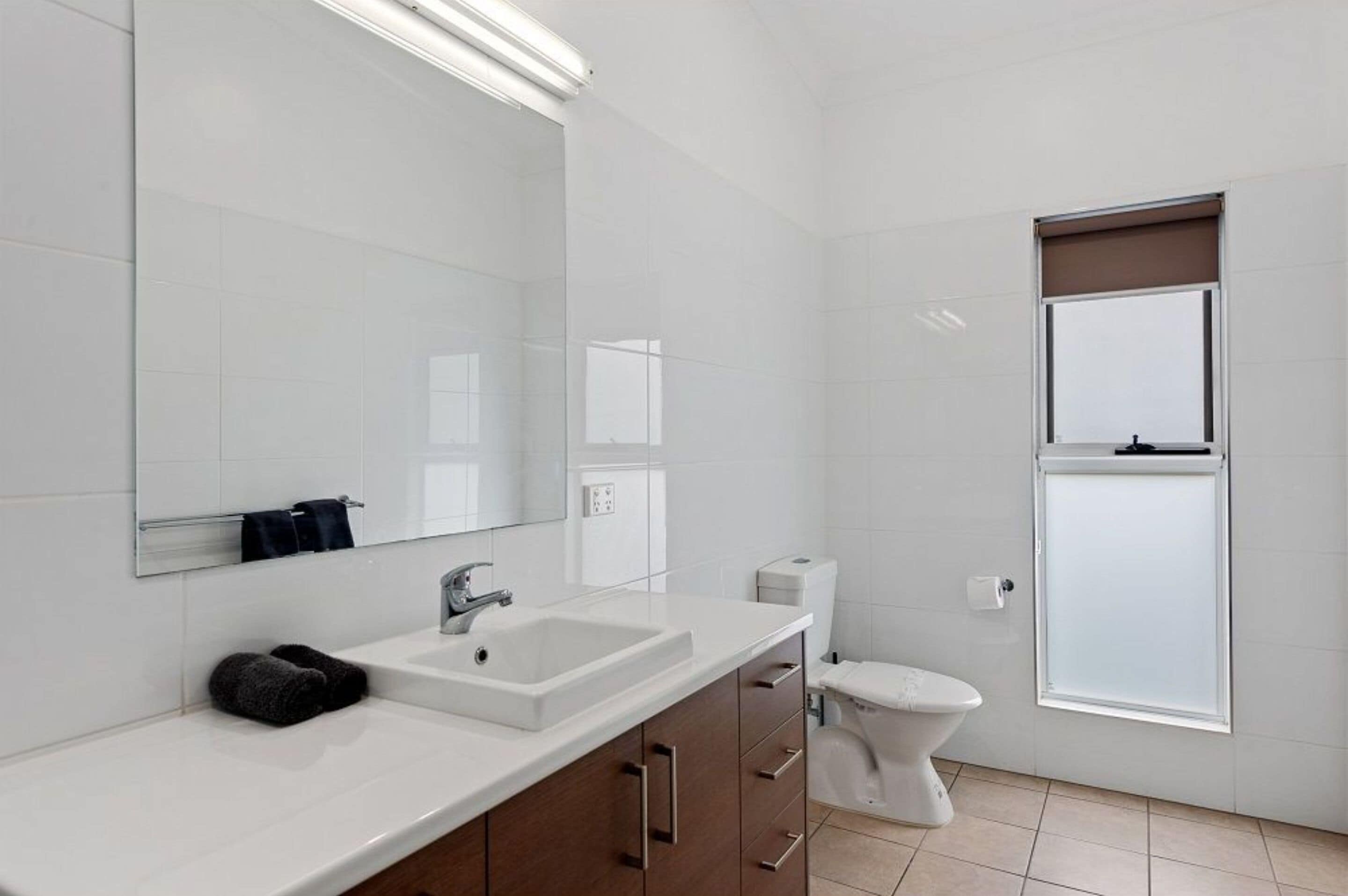 Un baño moderno con lavamanos, espejo y retrete blancos.
