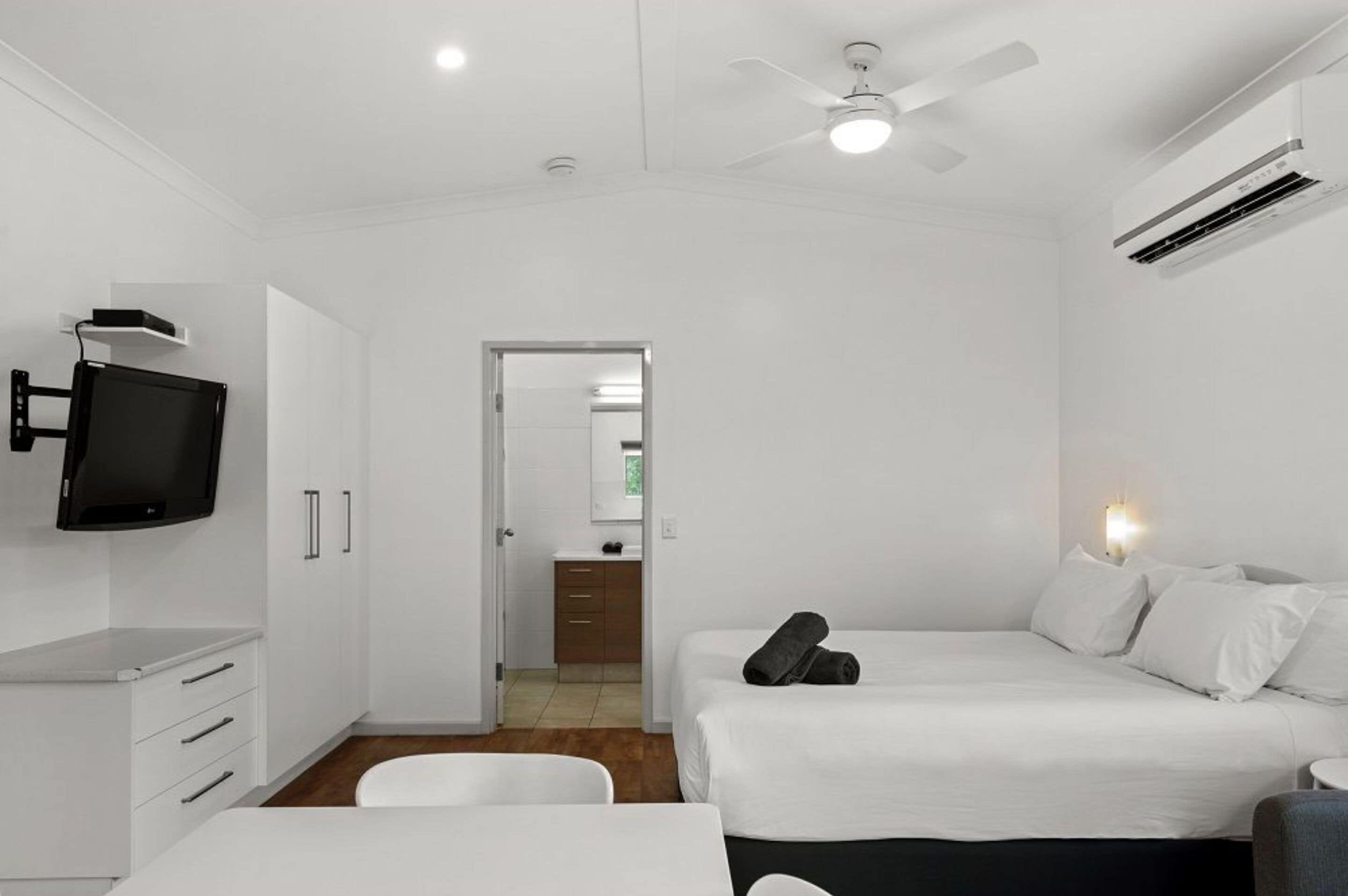 A modern hotel room with a bed, a desk, a chair, a television, and a ceiling fan.