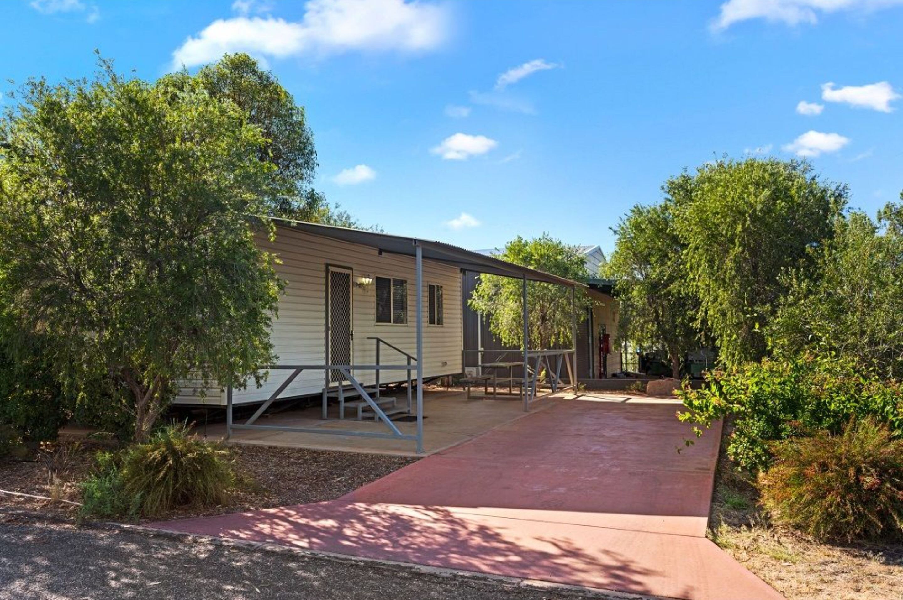 A mobile home with a covered porch, surrounded by trees and a paved walkway.
