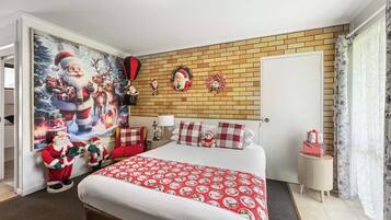 Un dormitorio con una cama grande, pared con diseño de ladrillos, una puerta, mesita de noche pequeña y decoración navideña en la pared.