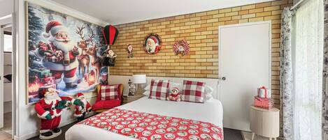 A bedroom with a large bed, a brick-patterned wall, a door, a small bedside table, and a wall with Christmas decorations.