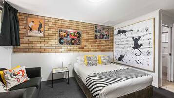 Una habitación de hotel moderna con una pared decorativa de ladrillo, una cama con ropa de cama a rayas, una mesita de noche pequeña y una silla con cojines de colores.