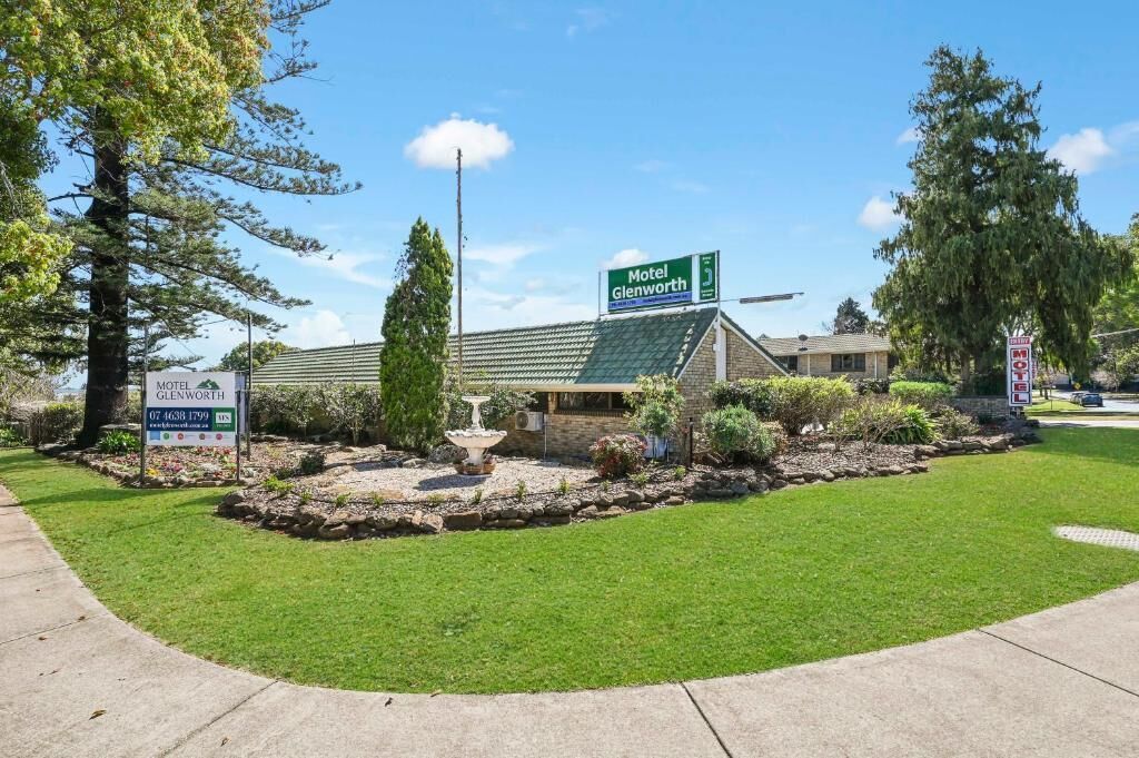 A motel with a green roof, a signboard, and a landscaped garden with a fountain.
