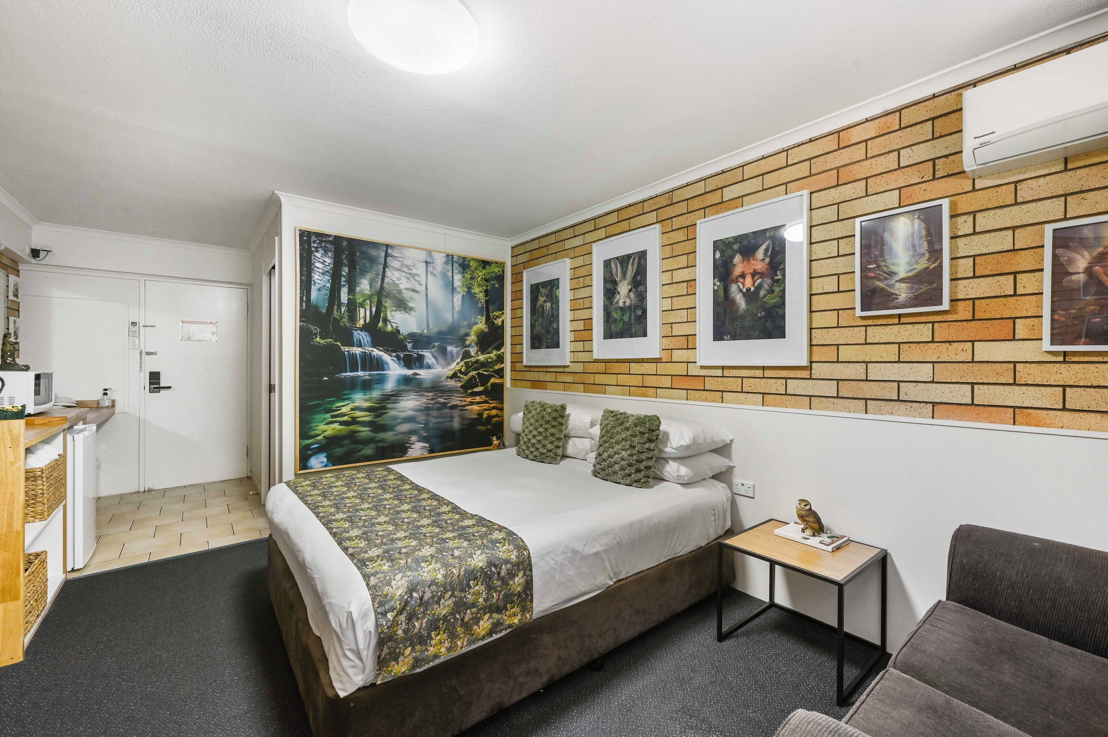 A hotel room with a bed, a small table, a sofa, a desk, and a wall with pictures.