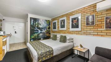 A hotel room with a bed, a small table, a sofa, a desk, and a wall with pictures.