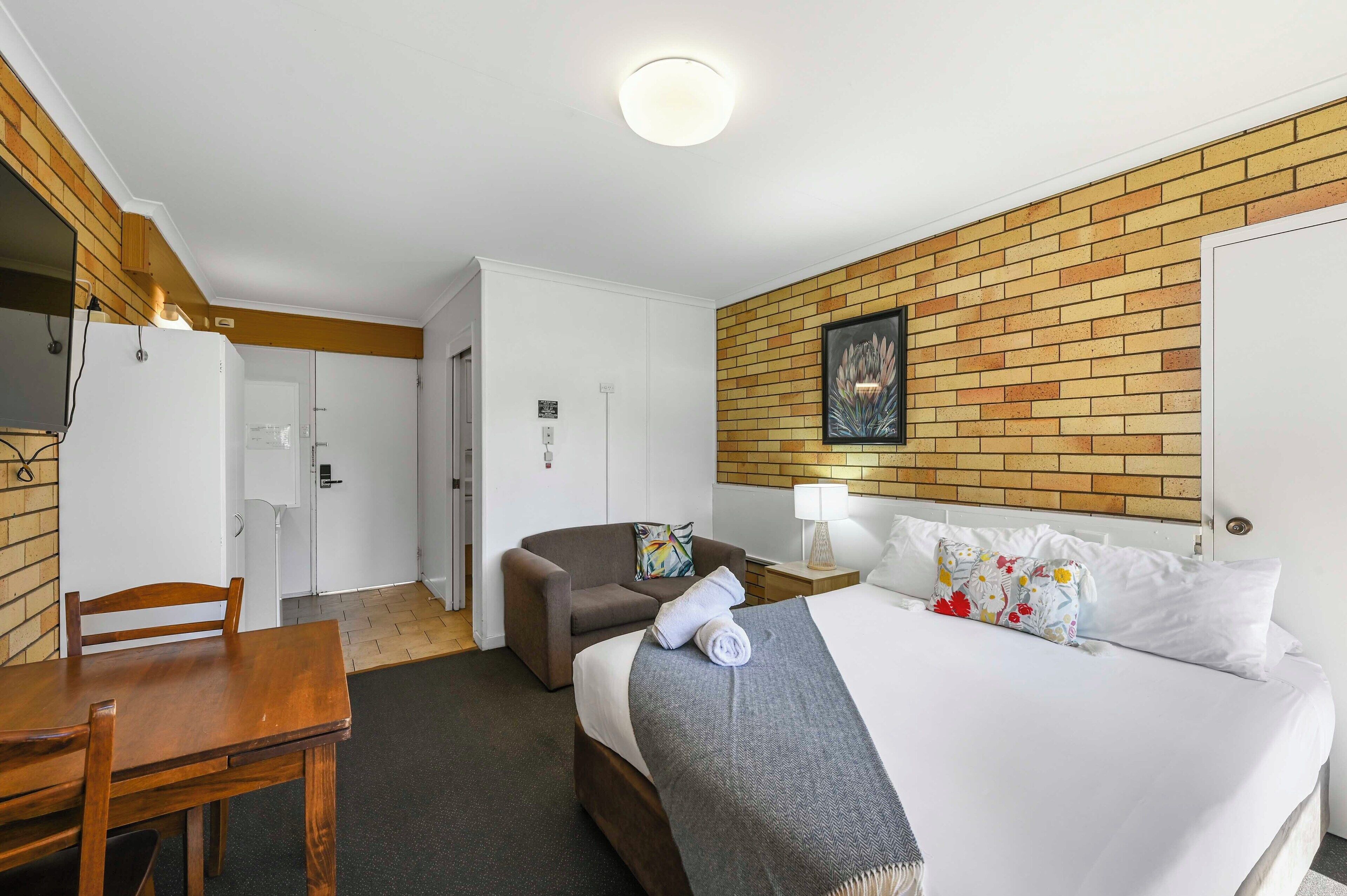 A hotel room with a bed, a desk, a chair, a small sofa, and a brick-patterned wall.