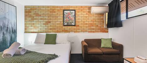 Ein Hotelzimmer mit einem Bett, einem braunen Sofa, einem kleinen Tisch und einer Wand-Klimaanlage.