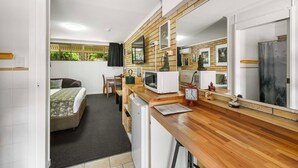 A compact room with a bed, a small kitchenette, a wooden counter, and a mirror.