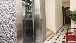 Un ascensor con pared de mosaico, una escalera con suelo de baldosas y una silla roja.
