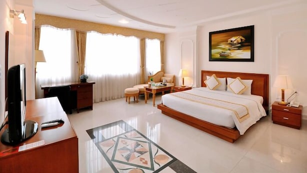 Habitación de hotel con una cama grande, un escritorio con ordenador, una silla, una mesita y un cuadro en la pared.