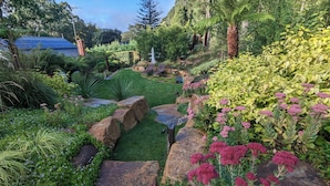 A landscaped garden with a variety of plants, rocks, and a pathway. - Garden Cottage at Fern Falls Cottages (Mount Dandenong)