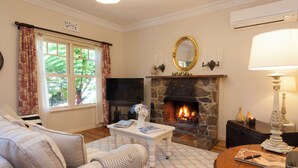 A cozy living room with a fireplace, a sofa, a coffee table, and a television. - Garden Cottage at Fern Falls Cottages (Mount Dandenong)