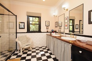Ein Badezimmer mit Schachbrettfußboden, zwei Waschbecken, einem großen Spiegel und einem Korbstuhl.