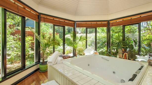 A spa room with a large bathtub, wooden flooring, and large windows offering a view of lush greenery. - Garden Cottage at Fern Falls Cottages (Mount Dandenong)
