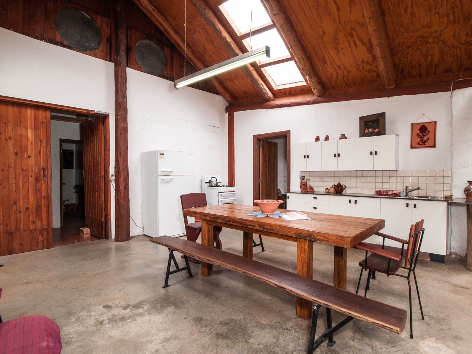 A rustic kitchen with a wooden table and benches, white cabinets, and a skylight.