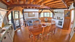 A spacious dining area with a wooden table and chairs, a kitchen with a stove and oven, and a cozy living area with a sofa and chairs. - Barkala Farmstay (Dandry)