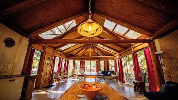 A spacious room with a high wooden ceiling, large windows, a central table with a decorative bowl, and a cozy seating area. - Barkala Farmstay (Dandry)