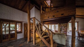 A rustic wooden interior with a stone-tiled floor, a wooden staircase, and a bookshelf filled with books. - Barkala Farmstay (Dandry)