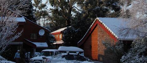 A residential area with houses covered in snow, a car parked in front, and a person standing near the entrance.
