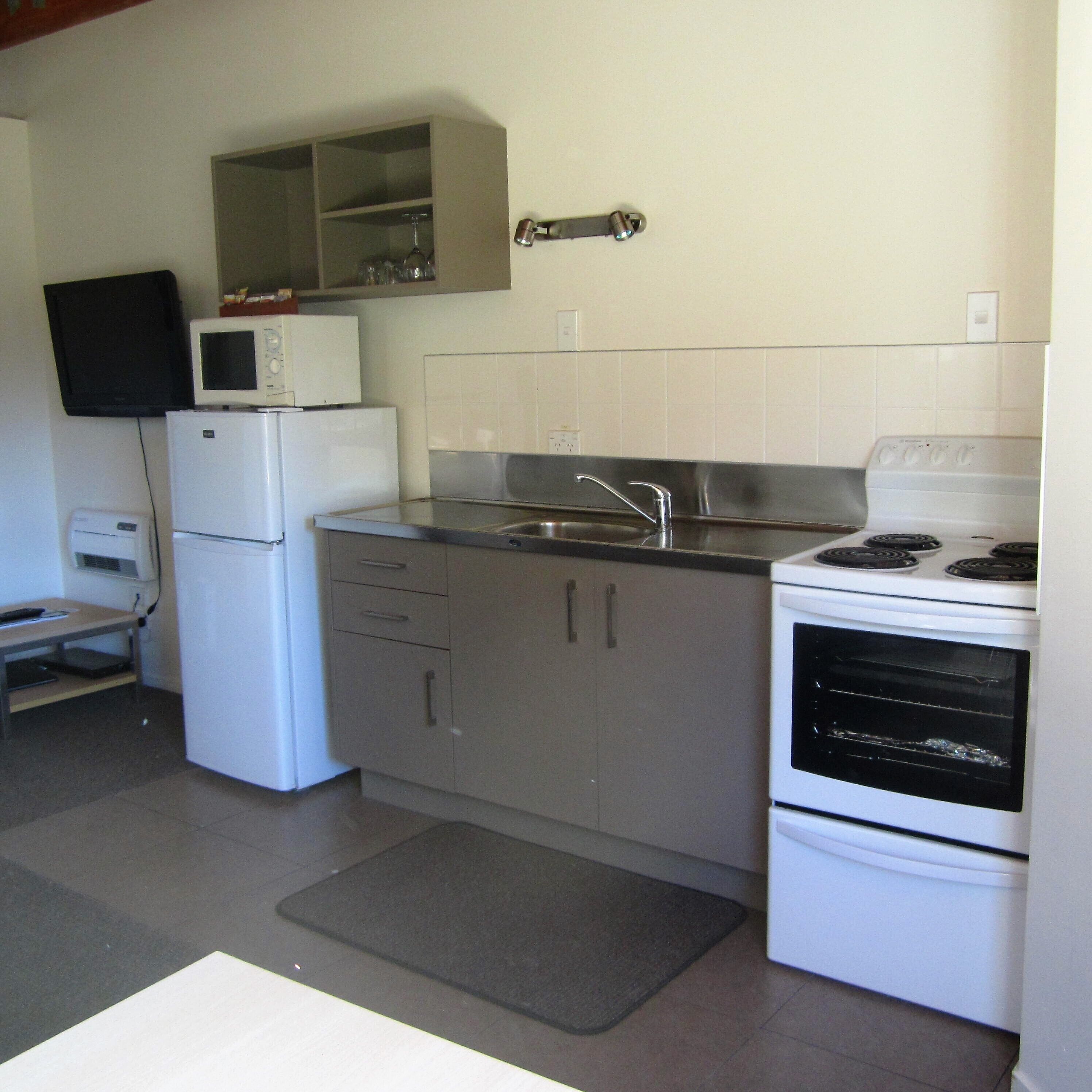 A compact kitchen with a refrigerator, microwave, stove, and sink.