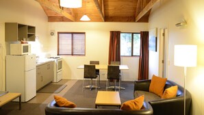 Un espacio habitable compacto con kitchenette, comedor y zona de estar con sofá y sillones.