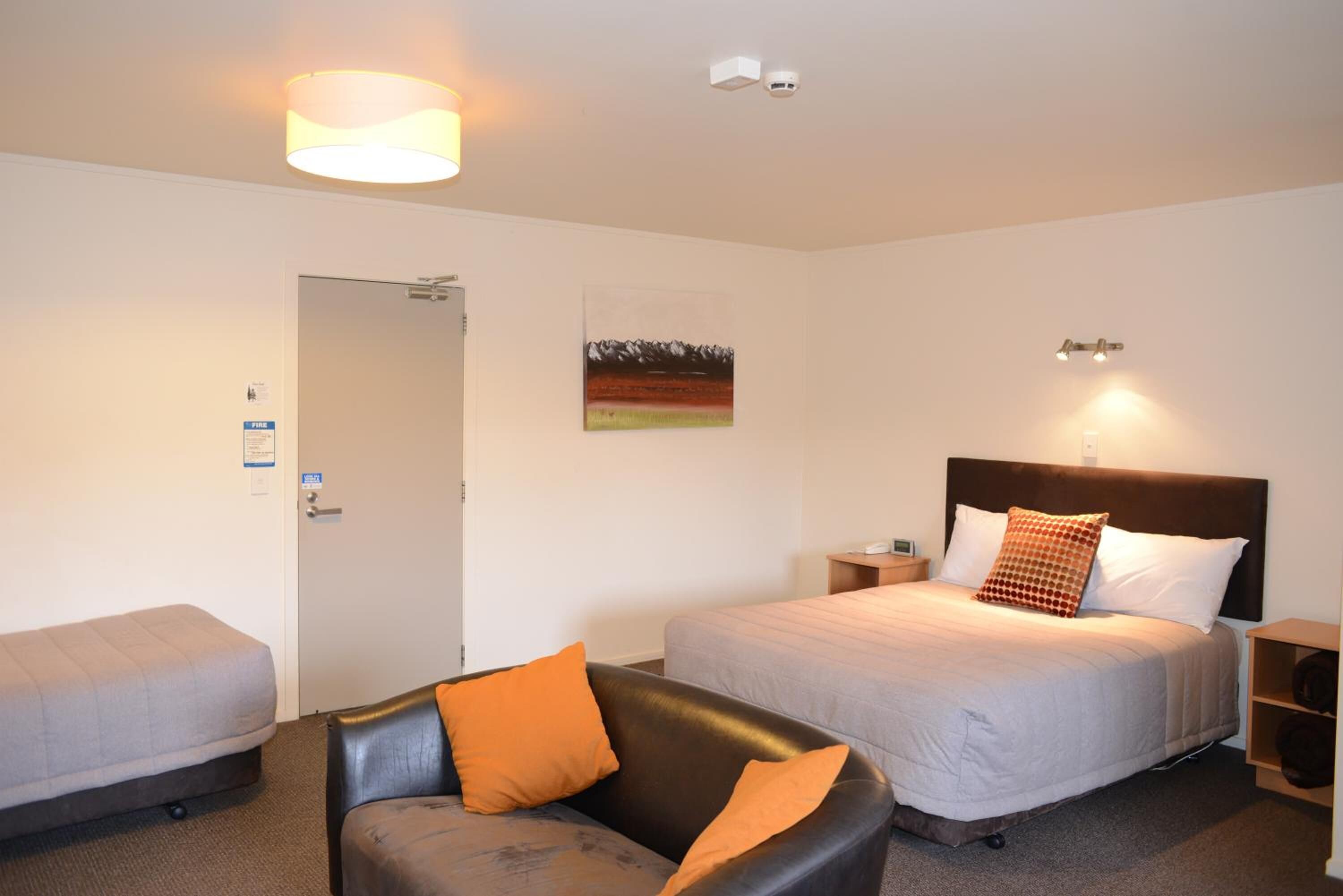 Hotellihuone, jossa on sänky, tuoli, yöpöytä ja lamppu.