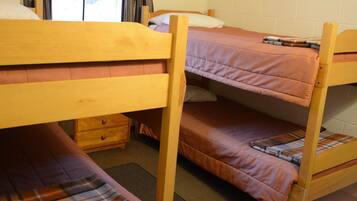 Camera con letto a castello, una testiera in legno, un piccolo comò di legno e una coperta a quadri sul letto inferiore.