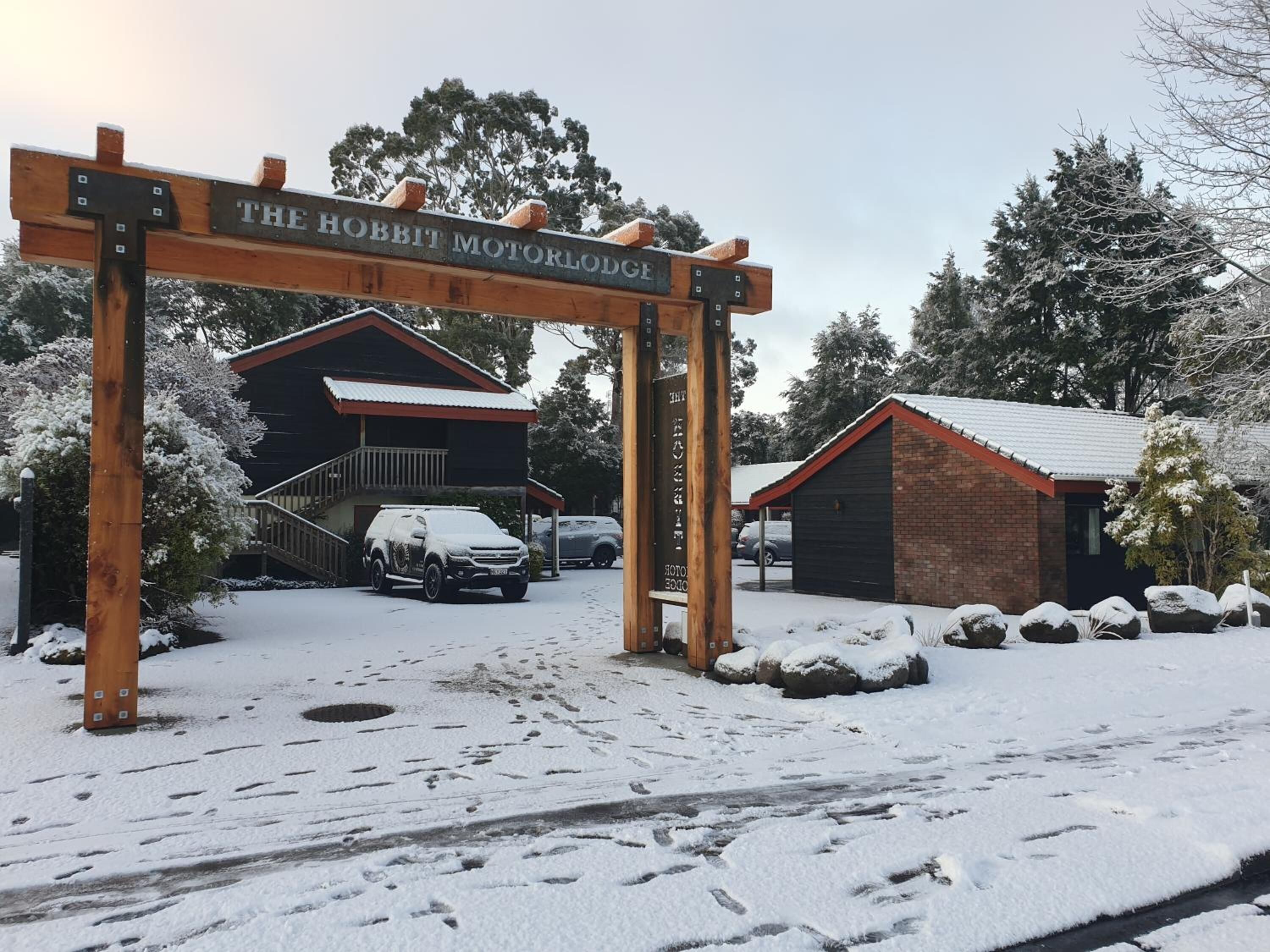 Un cartello di legno con la scritta "The Hobbit Motor Lodge" e un edificio sullo sfondo.