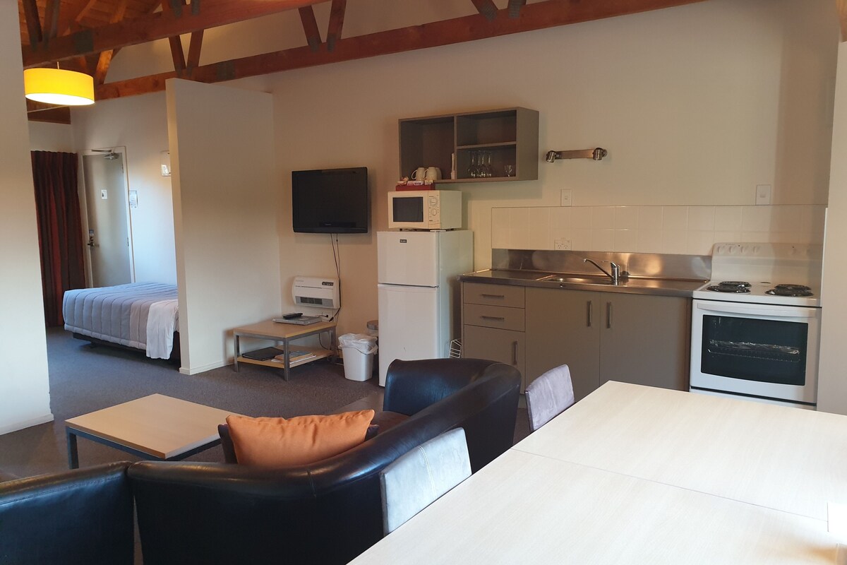 A compact living space with a kitchenette, a bed, a television, and a dining area.