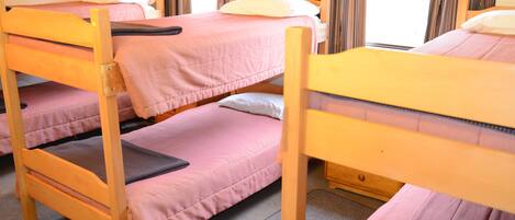A dormitory room with bunk beds, wooden headboards, and a window with curtains.