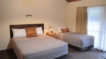 A double bed with a wooden headboard and two pillows, a bedside table with a lamp, and a window with curtains.