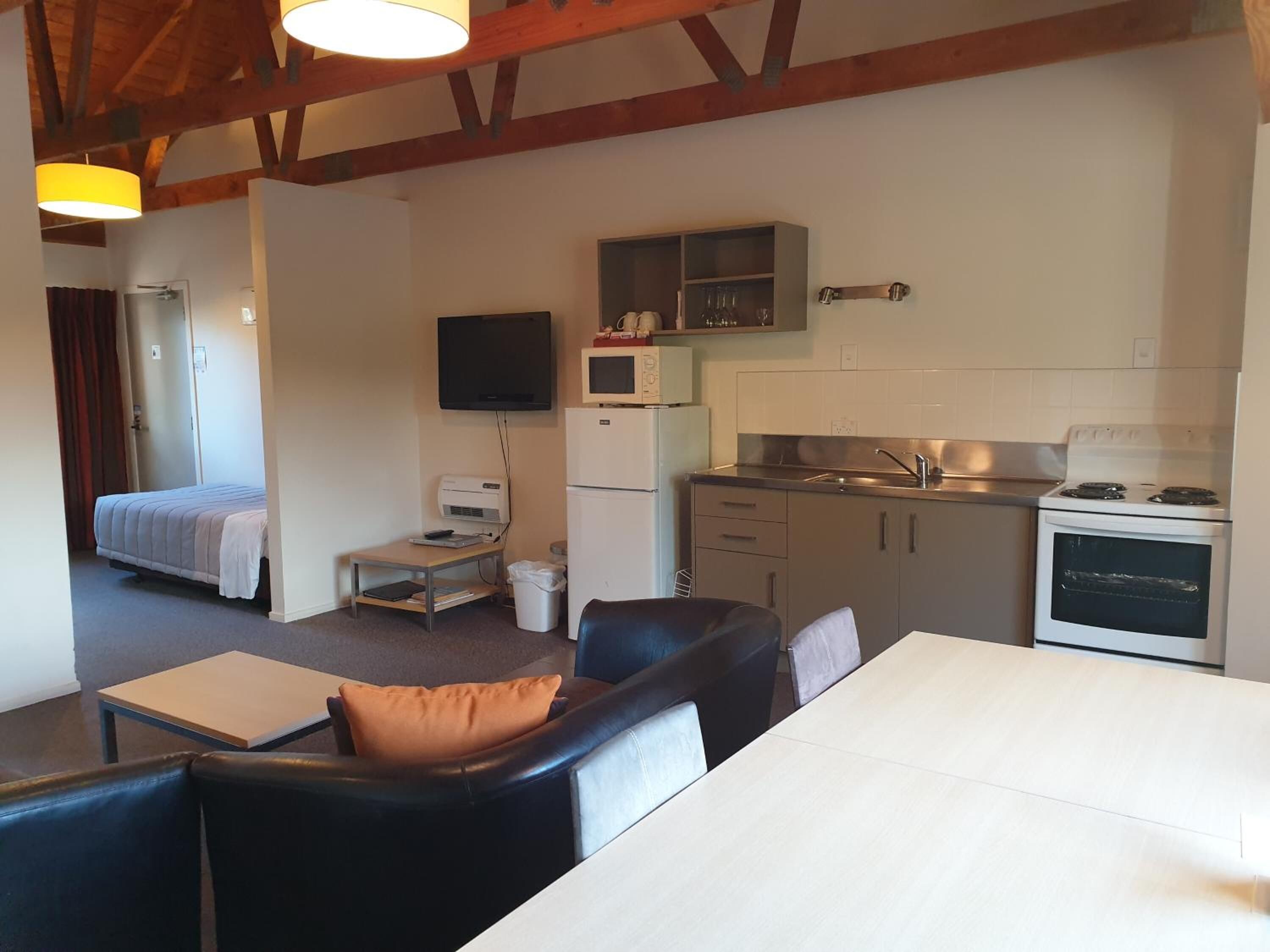 A compact living space with a kitchenette, a bed, a television, and a dining area with a table and chairs.