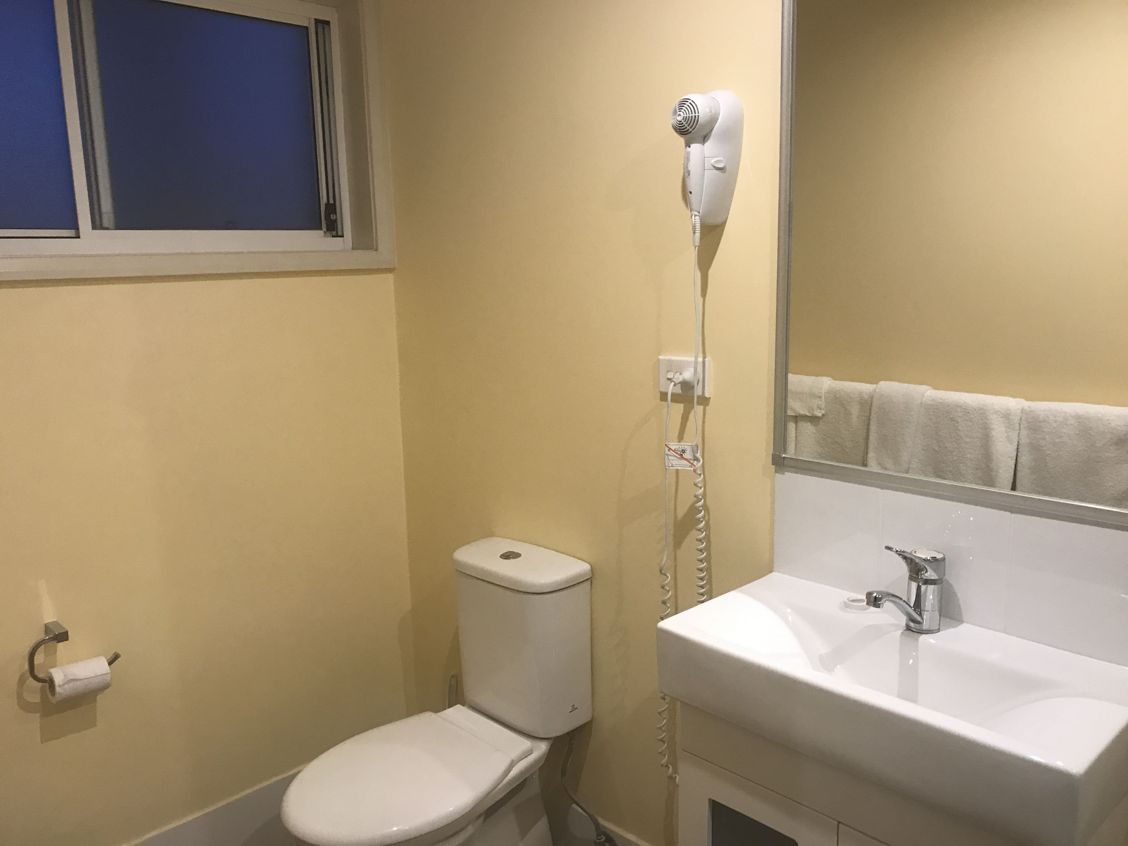 Un baño con inodoro, secador de pelo, lavabo y espejo.