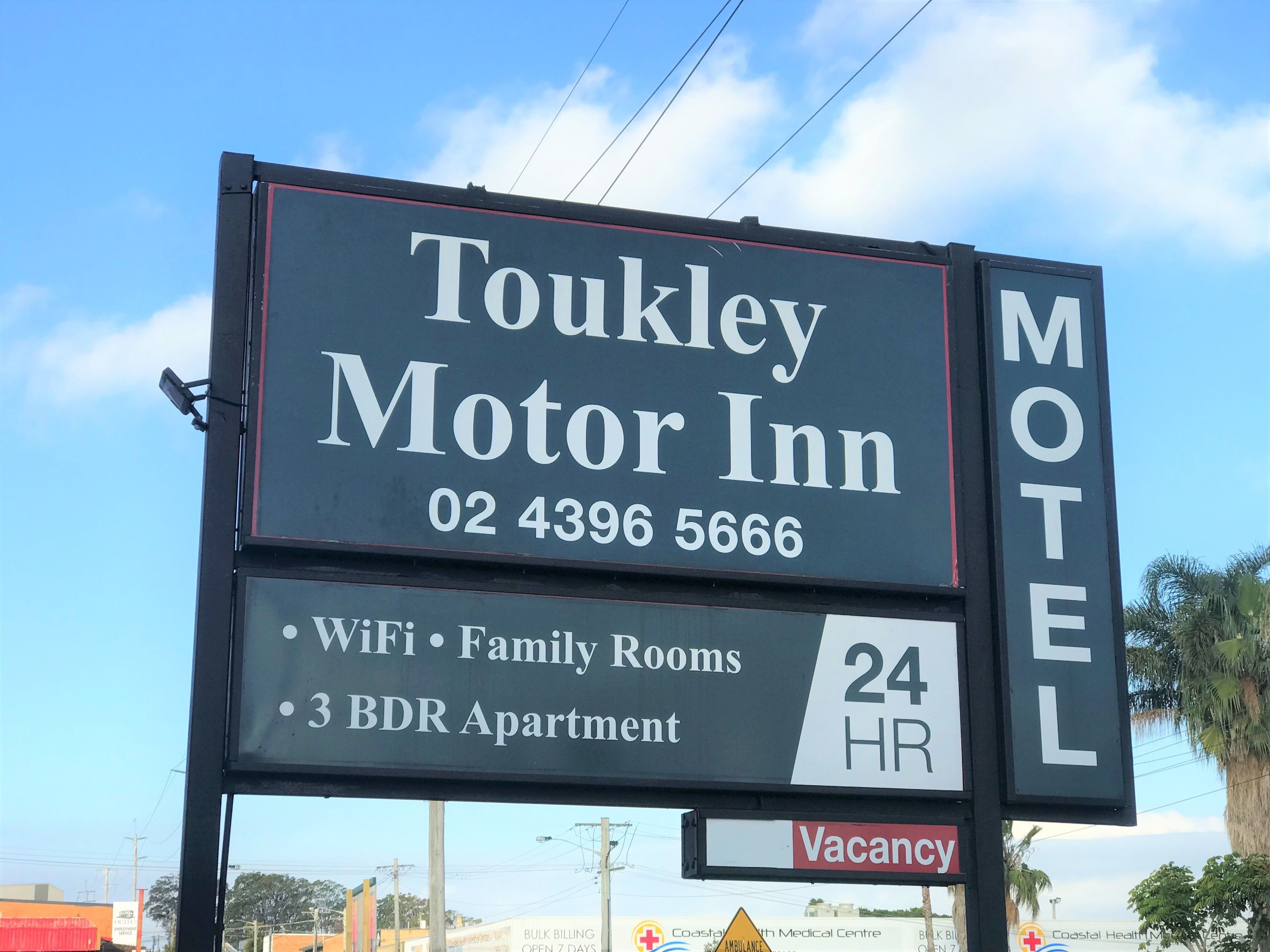 Toukley Motor Inn -hotellin kyltti, jossa luetellaan hotellin tarjoamat palvelut, kuten Wi-Fi, perhehuoneet, kolmen makuuhuoneen huoneistot ja ympärivuorokautinen palvelu.