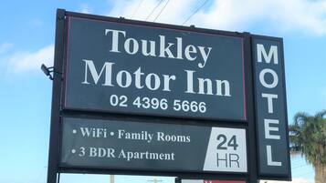 Toukley Motor Inn -hotellin kyltti, jossa luetellaan hotellin tarjoamat palvelut, kuten Wi-Fi, perhehuoneet, kolmen makuuhuoneen huoneistot ja ympärivuorokautinen palvelu.