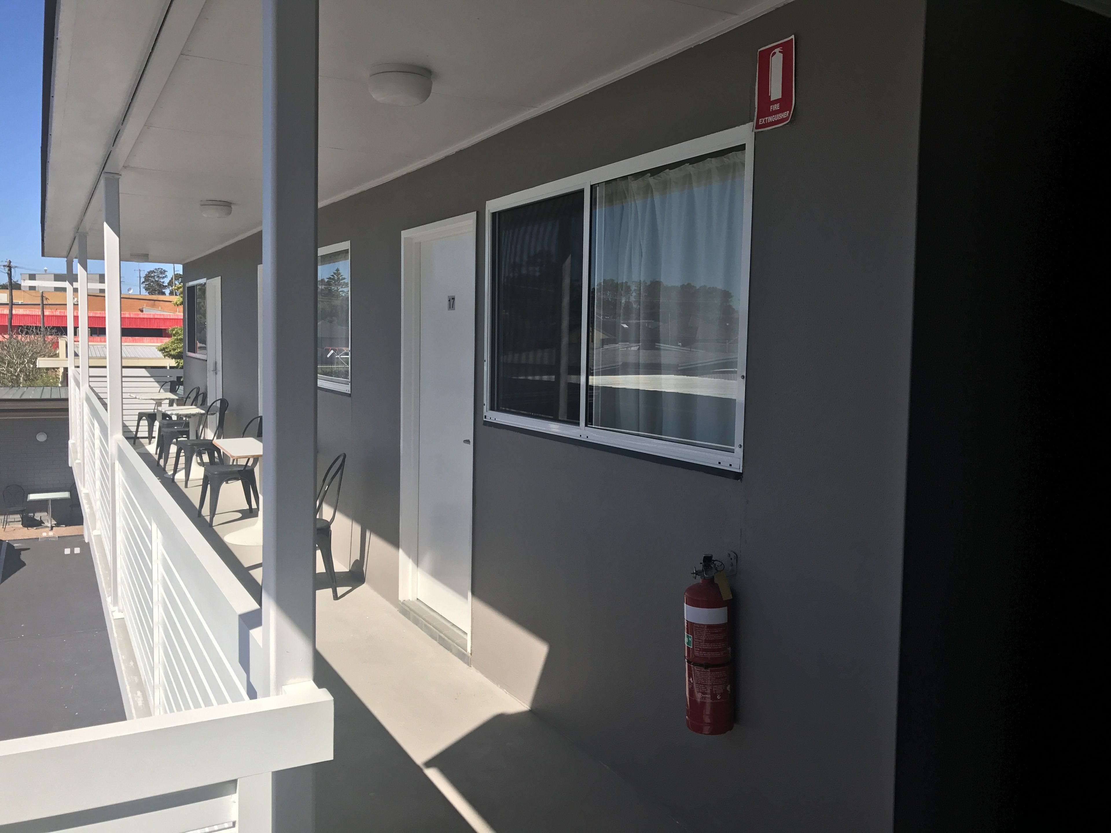 A balcony with outdoor seating, a fire extinguisher mounted on the wall, and a window with a curtain.