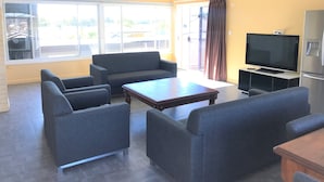 A living room with a sofa, armchairs, a coffee table, a flat-screen TV, and a refrigerator. - Toukley Motor Inn (Toukley)