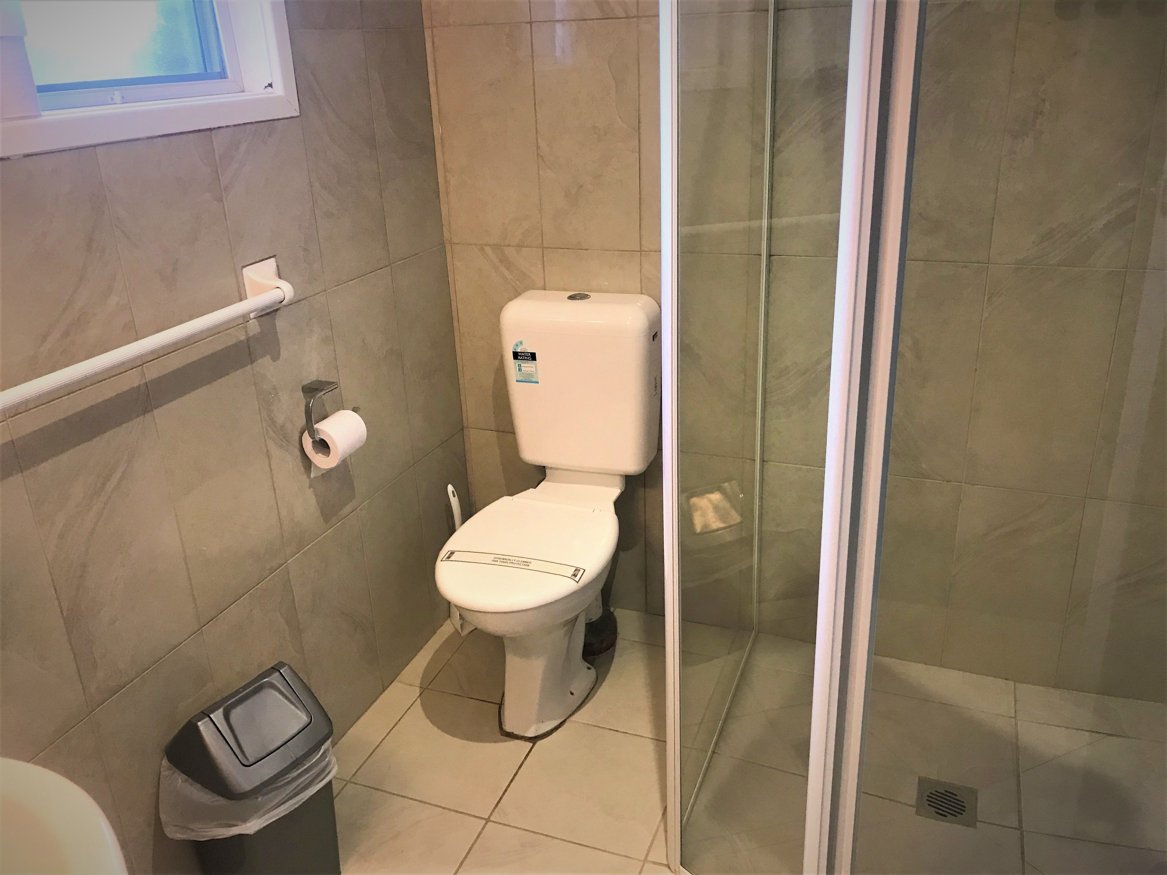 Baño con inodoro, un cubo de basura y una cabina de ducha de vidrio.