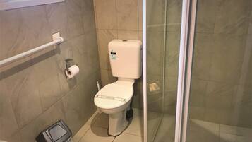 Baño con inodoro, un cubo de basura y una cabina de ducha de vidrio.