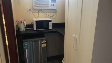 A compact kitchenette with a microwave, a small refrigerator, and a window-mounted air conditioner.