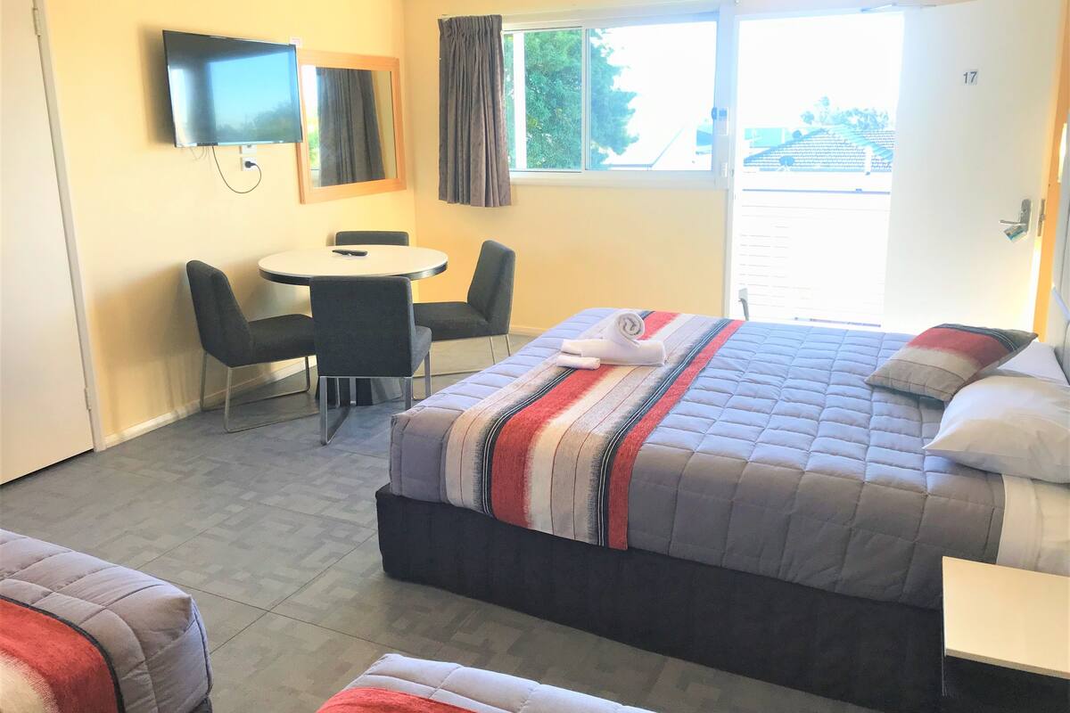 A hotel room with a bed, a desk, a chair, a TV, and a window with curtains.