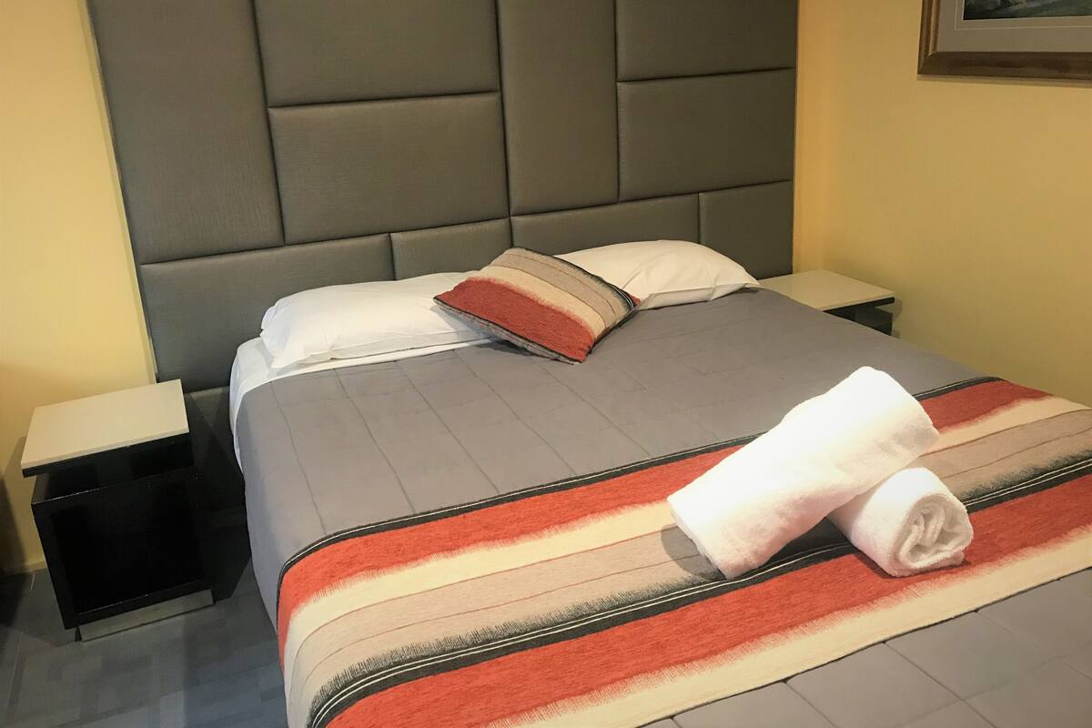 A neatly made bed with a striped blanket, pillows, and a rolled towel.