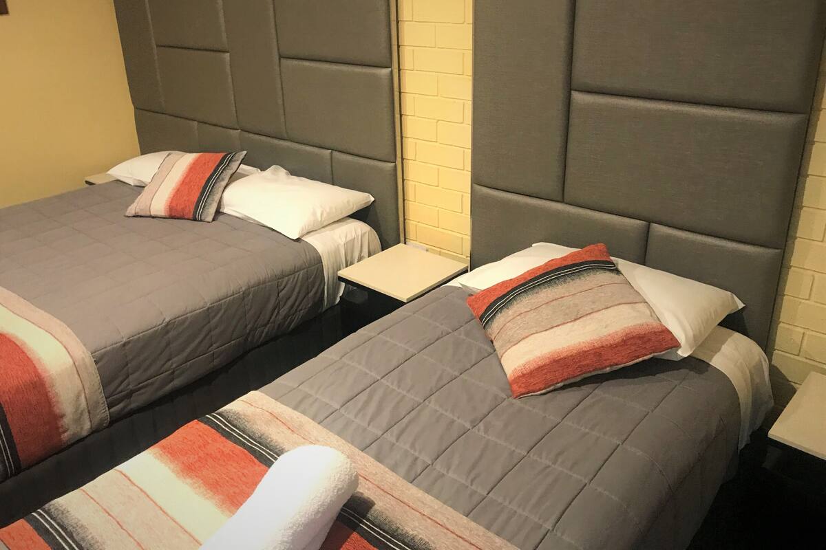 A hotel room with two beds, each with a grey headboard and a striped blanket.