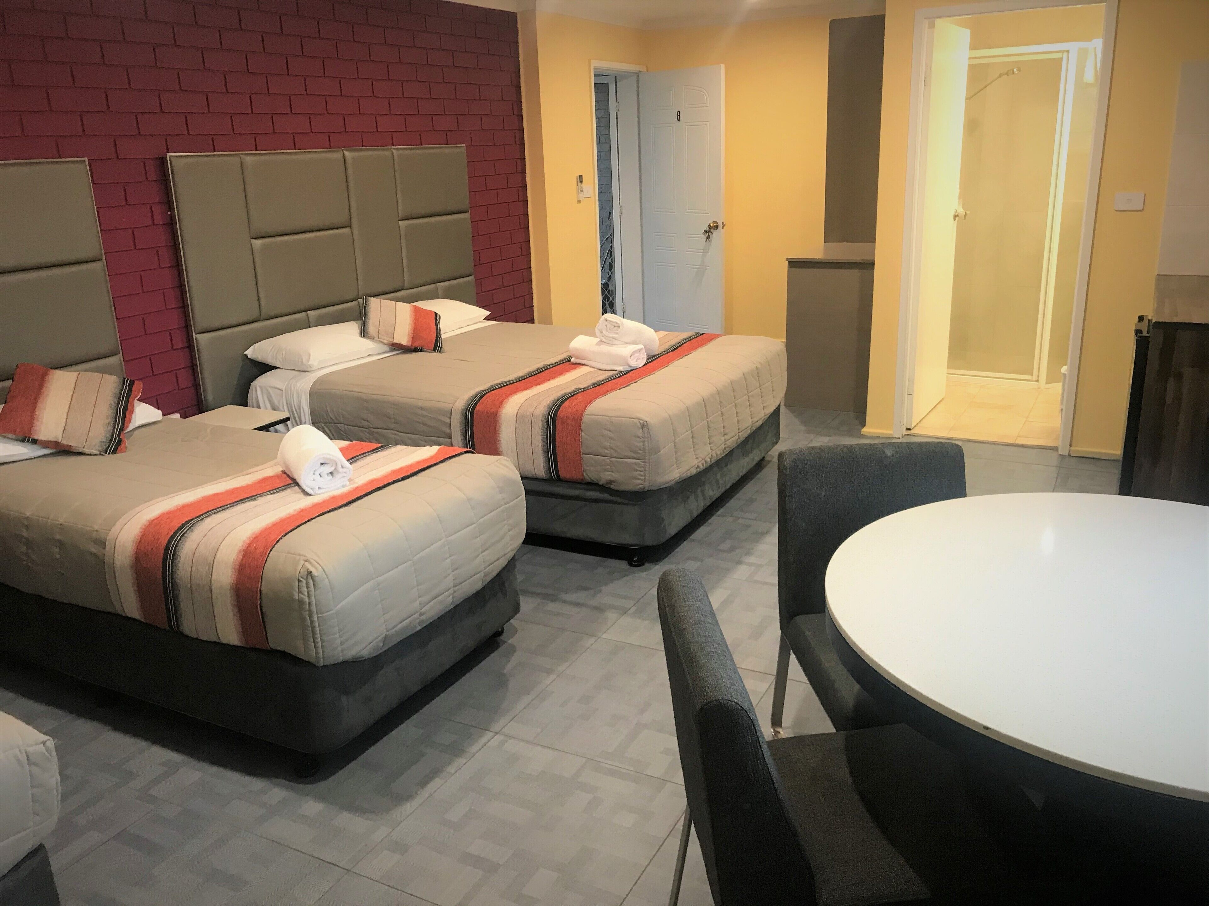 Habitación de hotel con dos camas, una mesa redonda y una pared de ladrillo.
