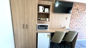 A compact kitchenette with a microwave, toaster, and small fridge. A TV is mounted on the wall, and there are two chairs and a small table. - Adrian Motel (Forbes)